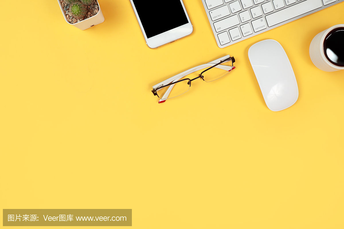 工作桌边有笔记本电脑,办公用品,咖啡杯,手机和咖啡杯在黄色的背景